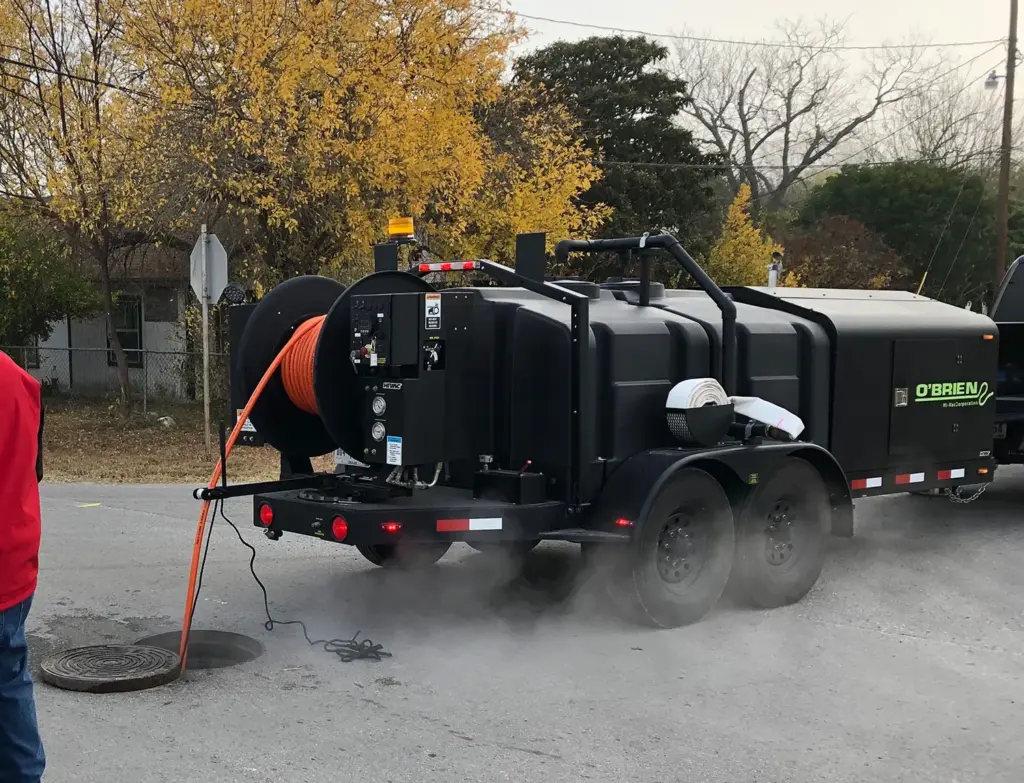 O'Brien Sewer Jetters trailer-mounted sewer jetter cleaning a city manhole with an orange hose.